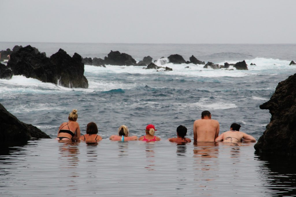Groupe de personnes assises au bord de l'eau, face à des vagues et des rochers.