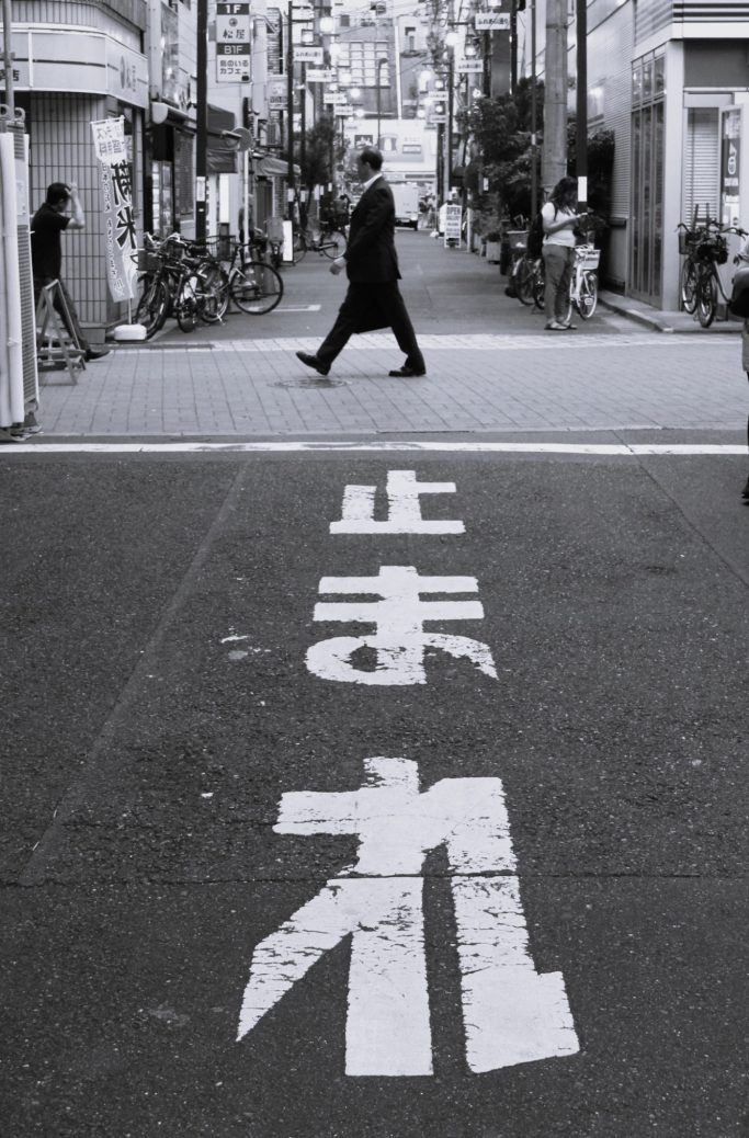 Homme en costume marchant sur une route avec une inscription en caractères japonais.
